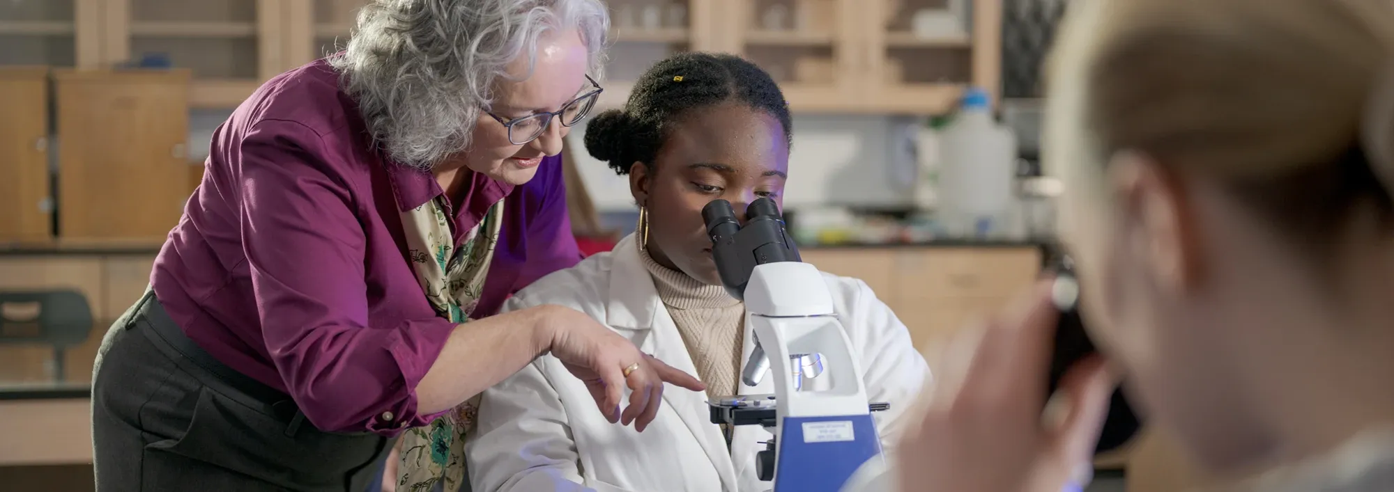 A biology professor showing a student details of a slide under a microscope